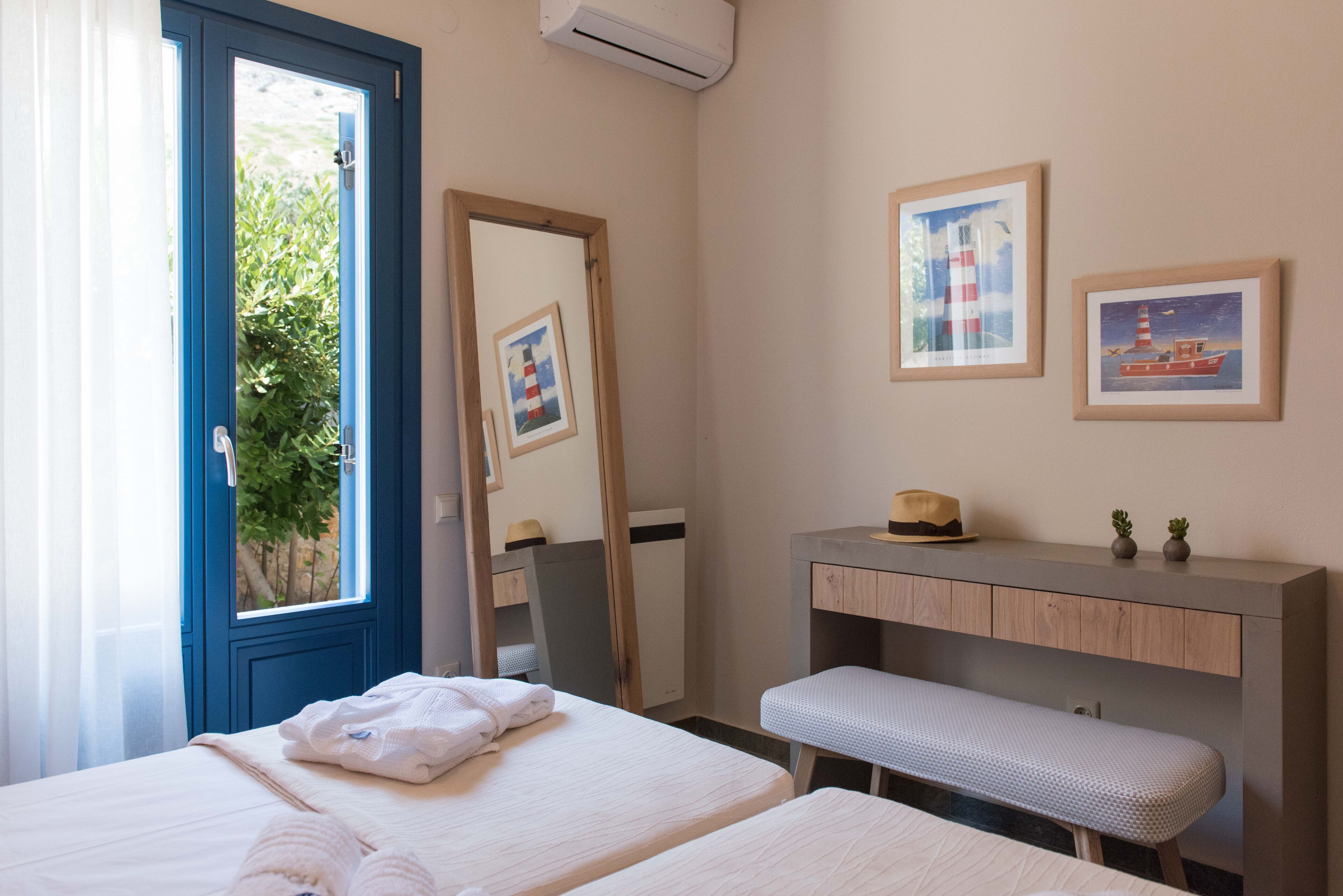 Une chambre d’hôtel avec deux lits, un banc, une coiffeuse avec un miroir et des tableaux encadrés au mur.