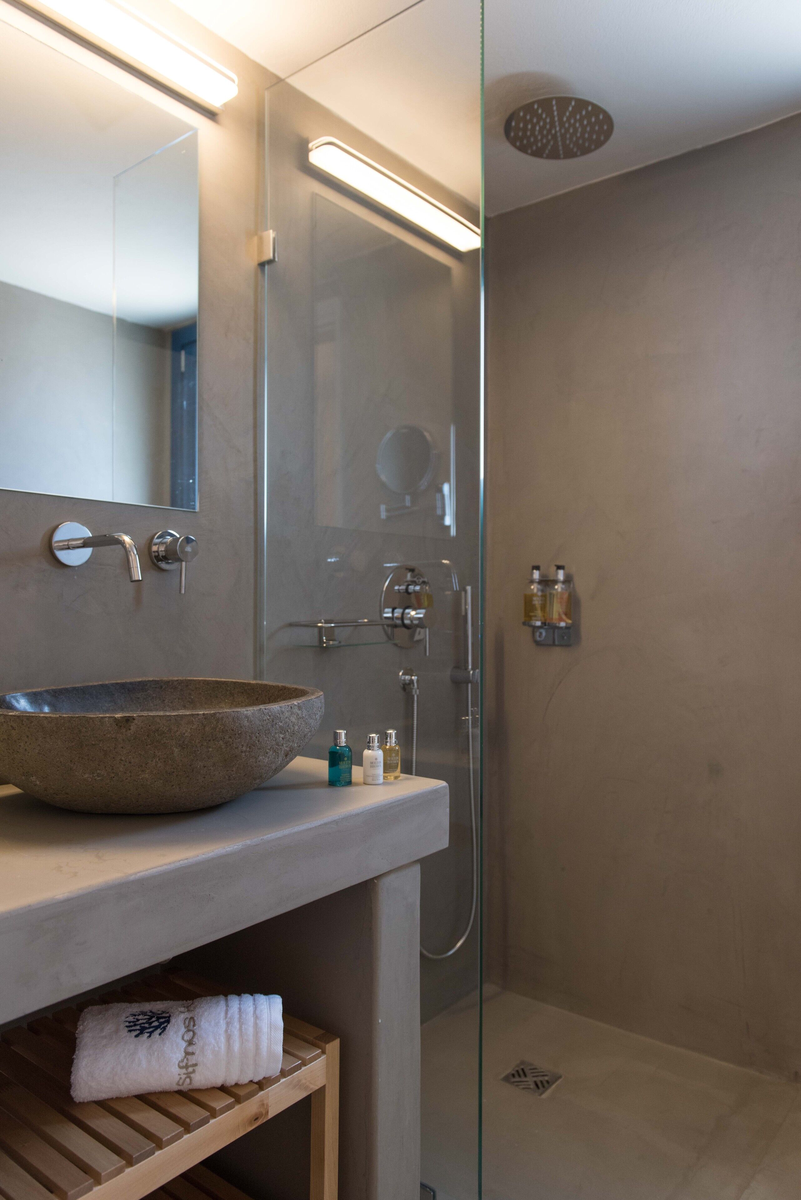 A modern bathroom with a large stone sink, a glass shower enclosure, and a wooden shelf with a towel.