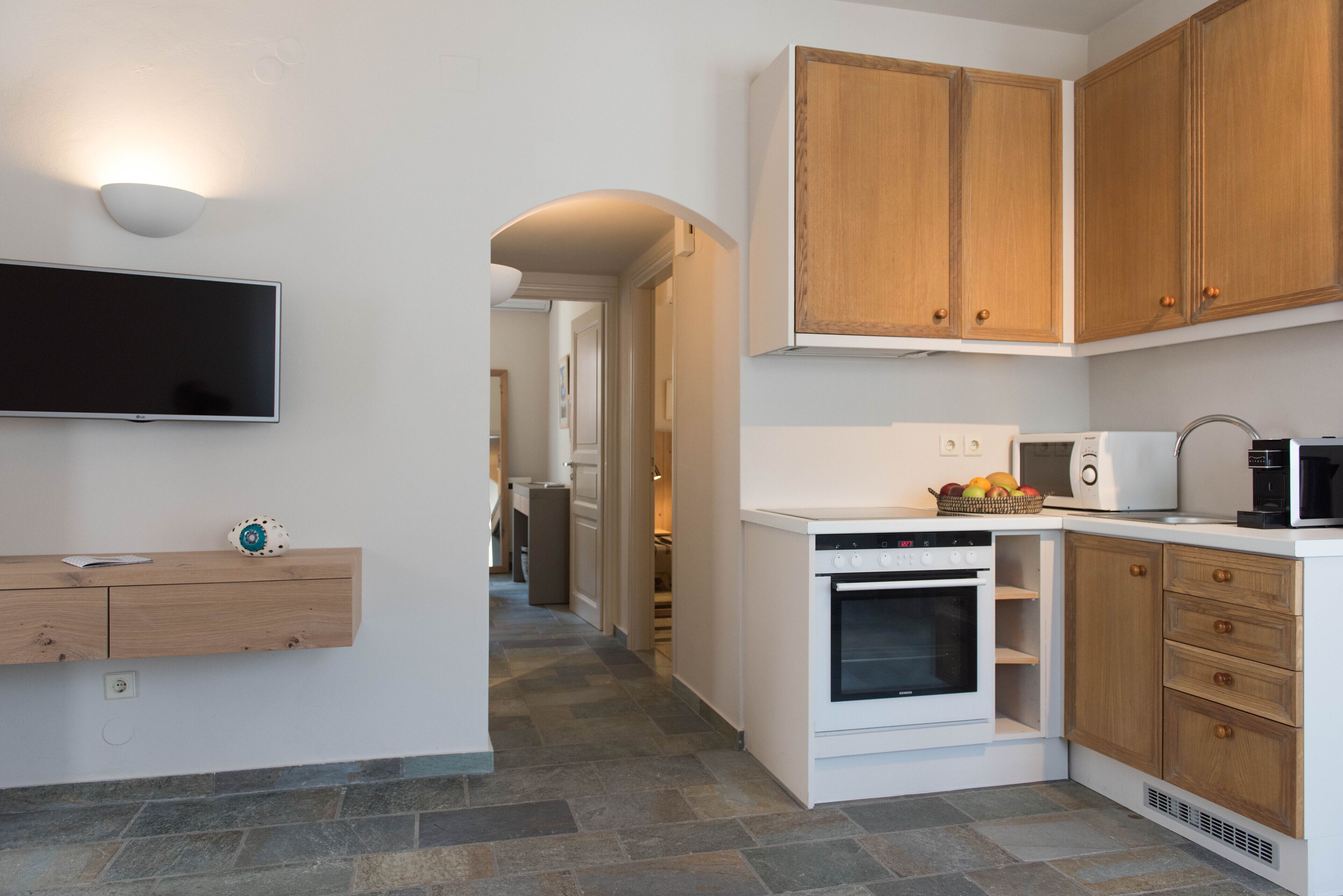 A modern kitchen with white cabinetry, a built-in oven, a microwave, and a countertop with fruit.