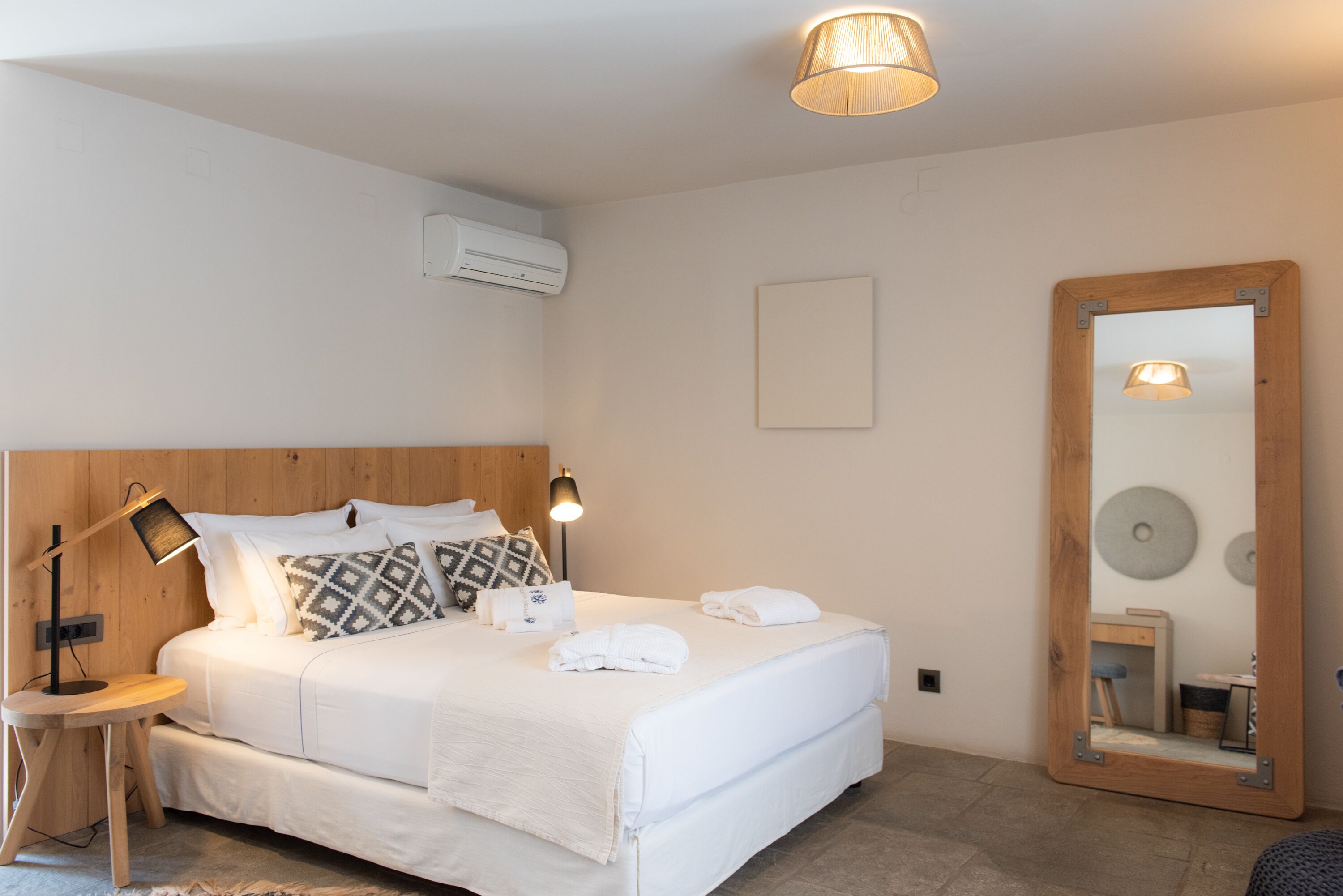 A neatly made bed with white linens, a bedside lamp, and a mirror with a wooden frame.