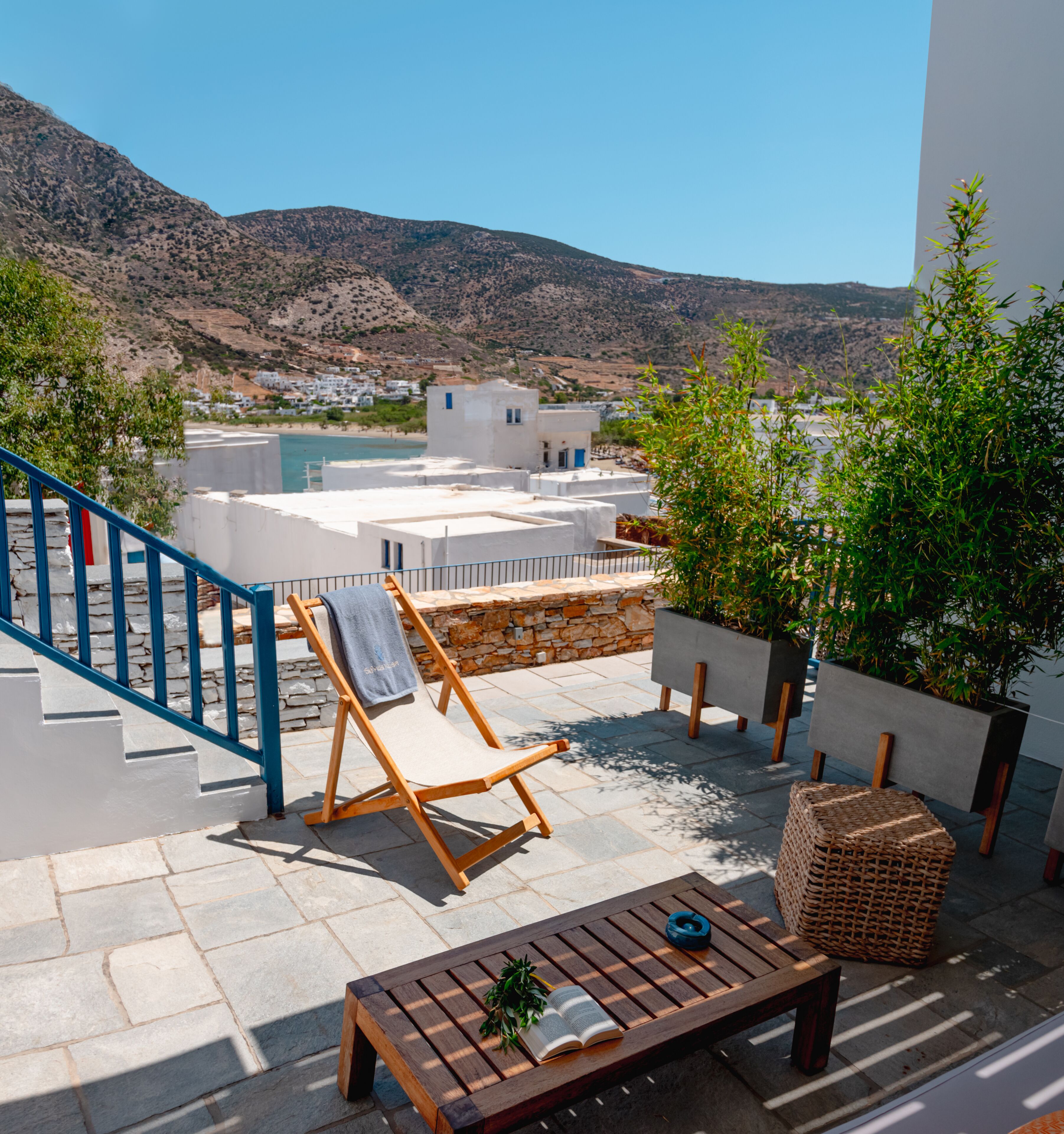 A terrace with a wooden chair, a bench, and a table with a book and a plant.