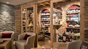 Una bodega acogedora con estantes de madera y pared de piedra, que exhibe una variedad de botellas de vino y un rincón de descanso con cojines rojos.