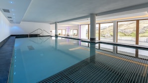 Una amplia piscina interior con paredes de vidrio transparente, suelo de baldosas y vistas a un paisaje montañoso.