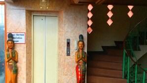 A hotel entrance with a marble wall, a door, and two statues of a figure in traditional attire. - Bliss Mansion (Pattaya)