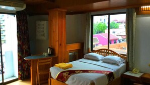 A room with a bed, a desk, a chair, and a window with a view of buildings. - Bliss Mansion (Pattaya)