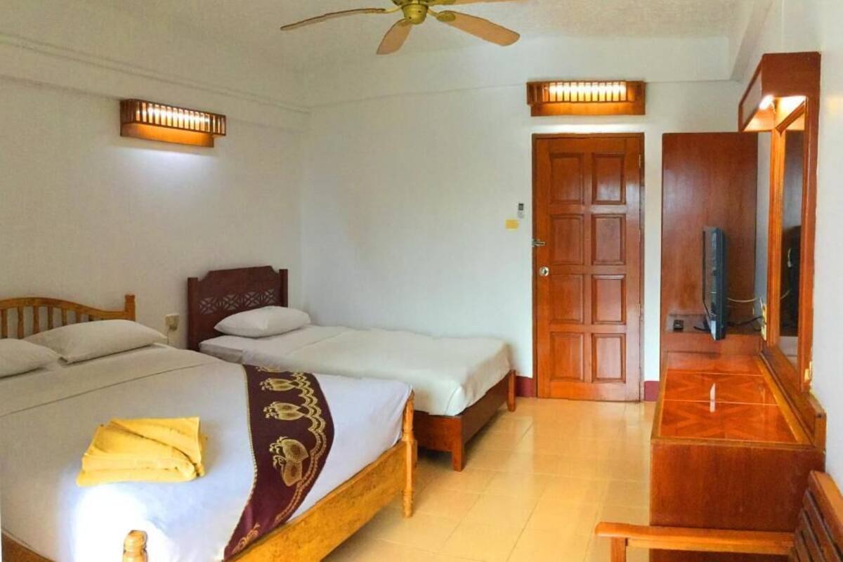 A hotel room with two single beds, a wooden headboard, a ceiling fan, a television, and a wooden dresser.