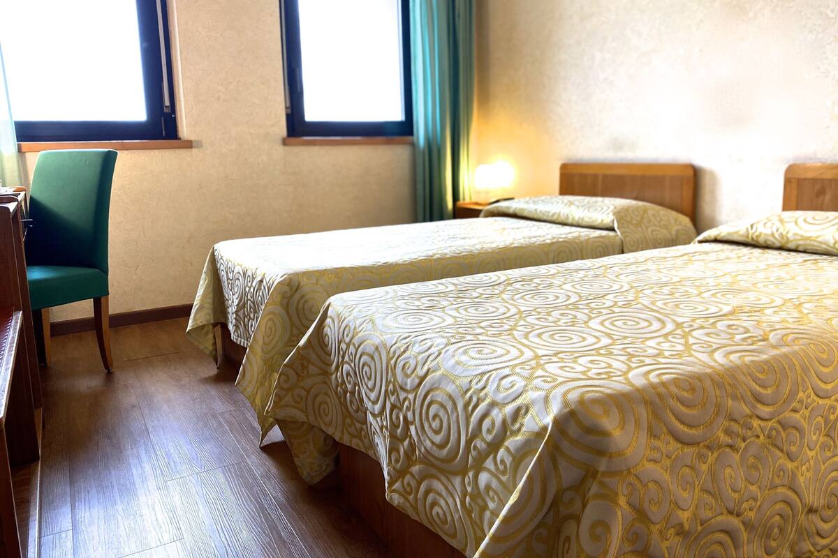 Ein Hotelzimmer mit zwei Einzelbetten, einem Schreibtisch und einem Stuhl.