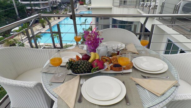 A dining table with breakfast items, a view of a swimming pool, and a balcony railing. - Westbury Residence (Pattaya)