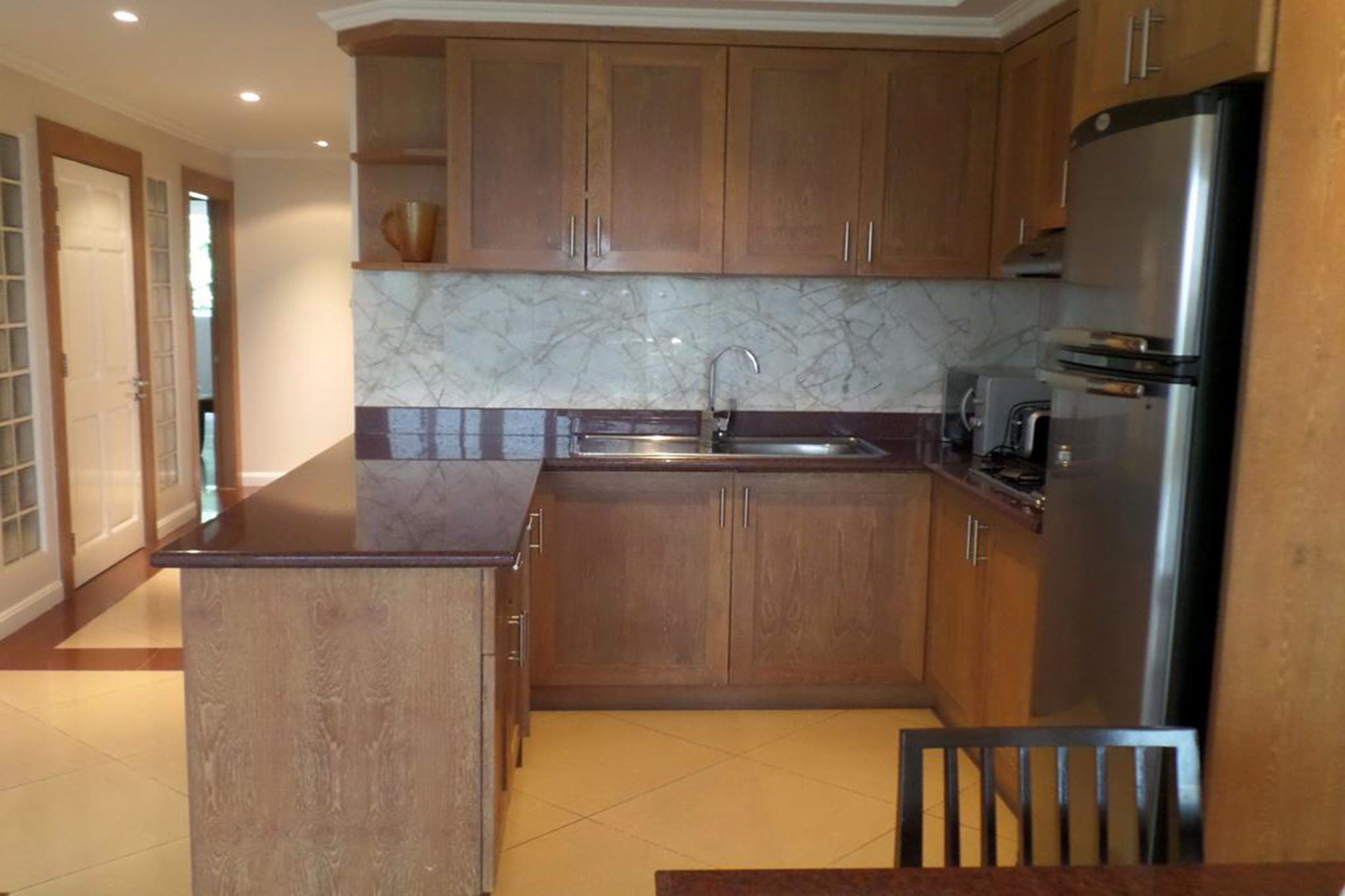 A kitchen with wooden cabinets, a marble backsplash, a stainless steel refrigerator, and a sink.