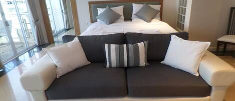 A modern hotel room with a large bed, a sofa, and a view of the outdoors.