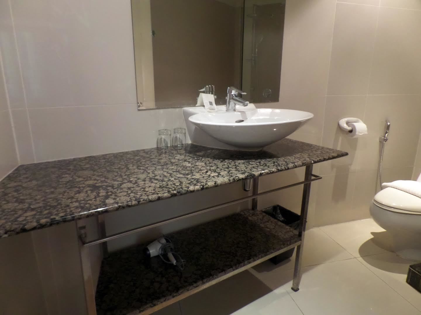 A bathroom with a granite countertop, a white sink, a mirror, a toilet, and a shower.