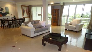 A spacious living room with a white sofa, a glass coffee table, and a dining area with chairs and a table. - Westbury Residence (Pattaya)