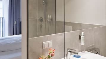 Ein modernes Badezimmer mit einer Duschkabine aus Glas, einem weißen Waschbecken und einem Spiegel, der den Raum reflektiert.