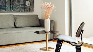 Una sala de estar moderna con un sofá gris, una mesa de centro redonda de vidrio con un jarrón blanco y una silla negra.