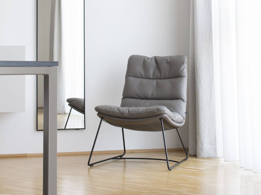 A modern room with a grey upholstered chair, a wooden floor, a white wall, and a large mirror.