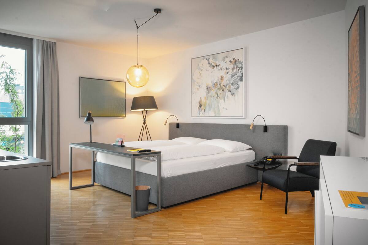 Une chambre d’hôtel moderne, équipée d’un lit, d’un bureau, d’une chaise et ornée d’œuvres d’art sur les murs.