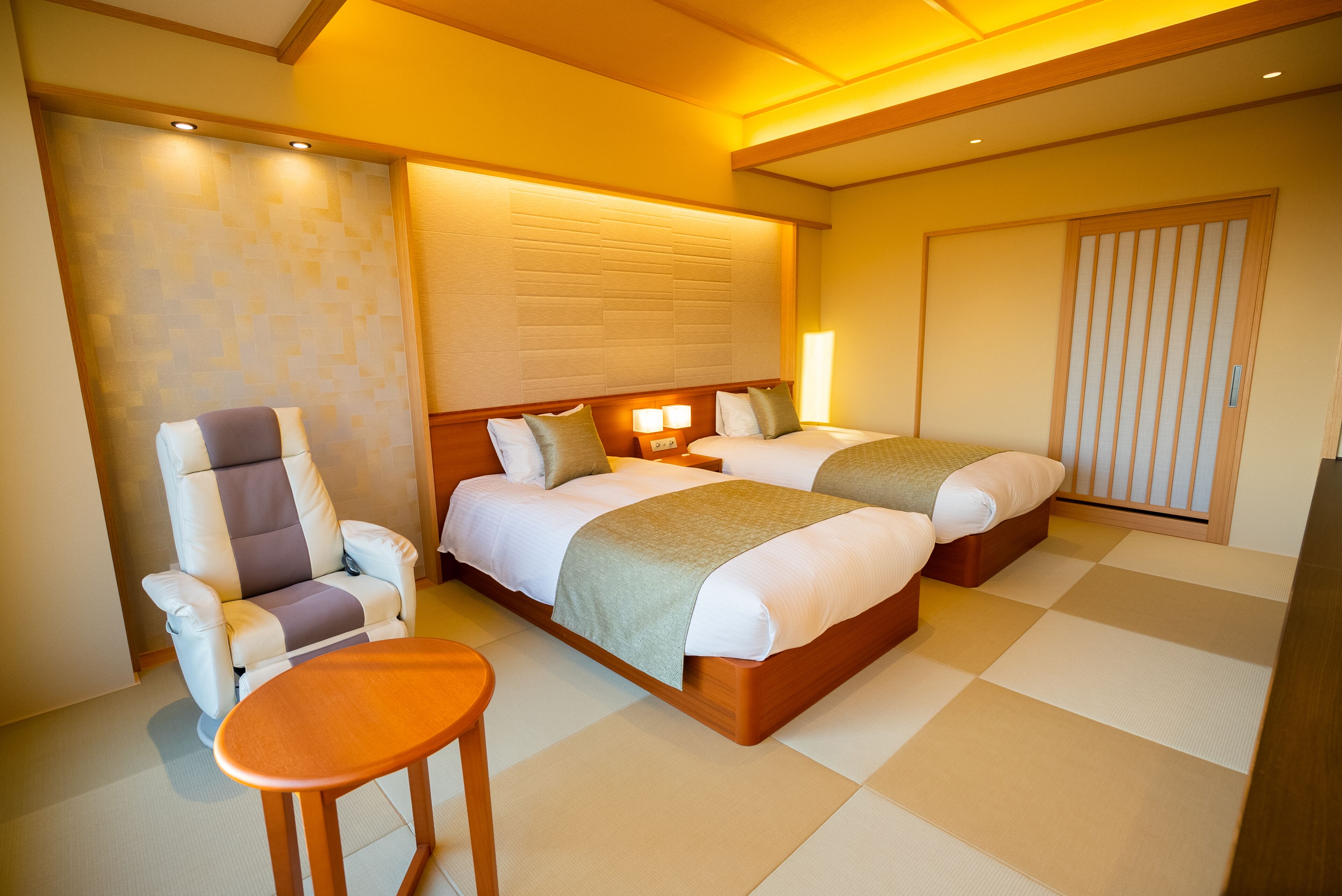 A hotel room with two beds, a sofa, a small table, and a wall-mounted TV.