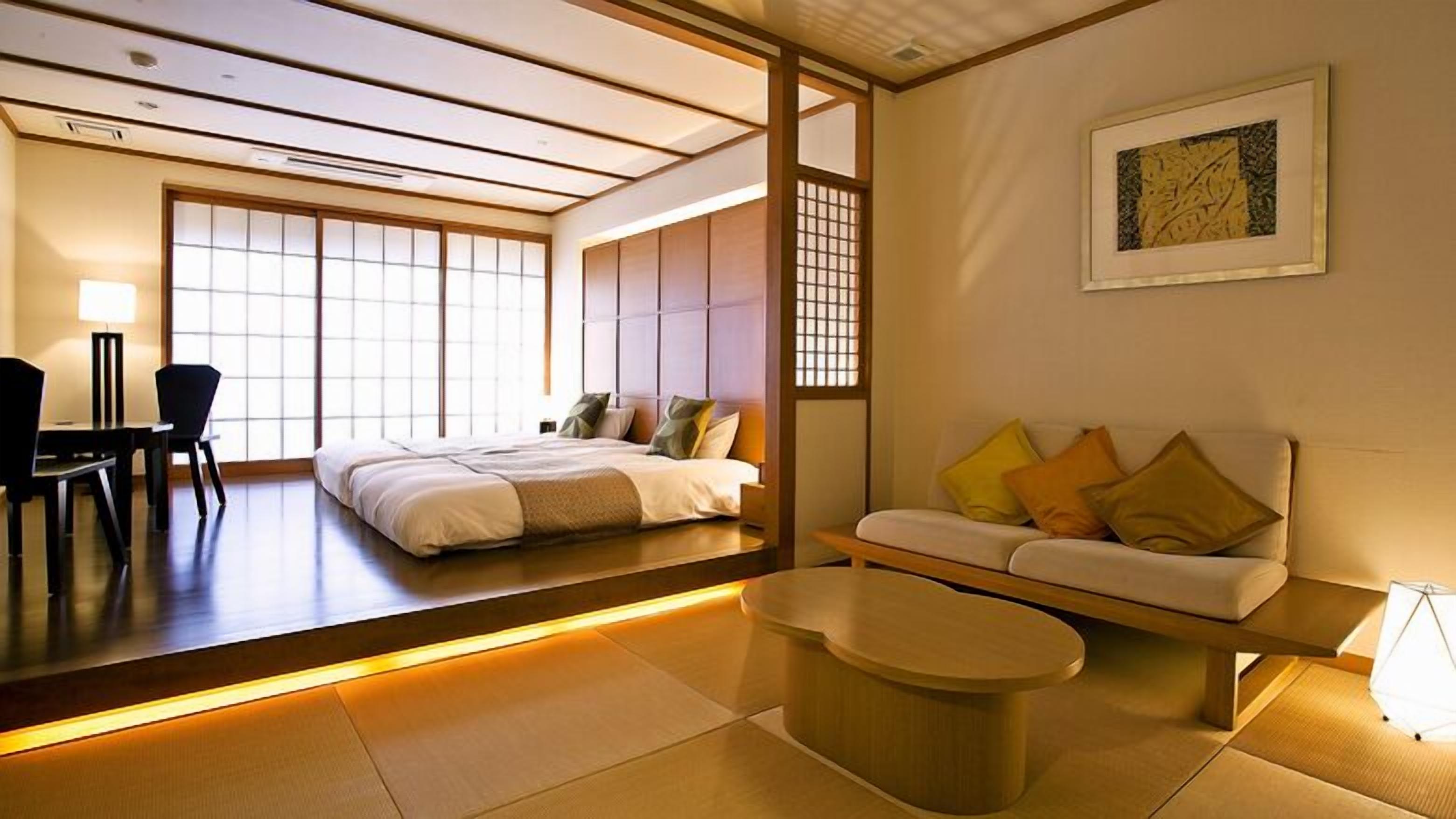 Une pièce de style japonais traditionnel, avec un sol recouvert de tatamis, un lit bas, un canapé avec des coussins, une petite table et une porte coulissante.