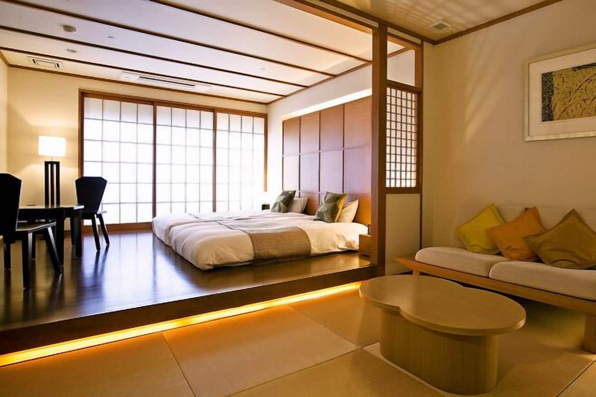 A traditional Japanese-style room with tatami flooring, a low platform bed, a sofa with cushions, a small table, and a sliding door.
