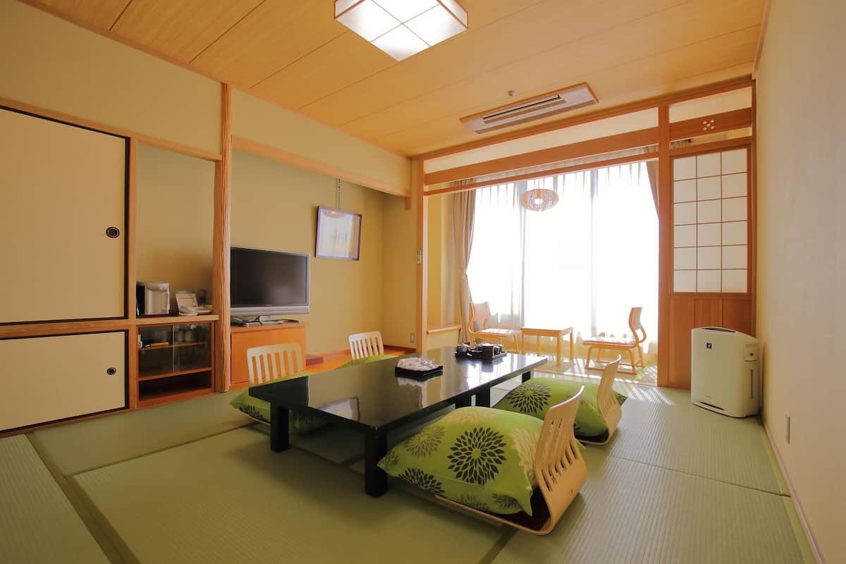 A traditional Japanese-style room with tatami flooring, a low table with cushions, a television, and sliding doors.
