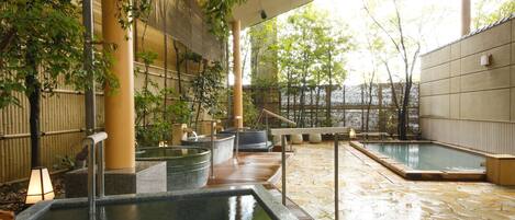 Un onsen japonés tradicional con baños de piedra, paredes de bambú y suelo de baldosas.