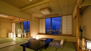 A traditional Japanese room with tatami flooring, a low table, cushions, and sliding doors. - Dogo Prince Hotel (Matsuyama)