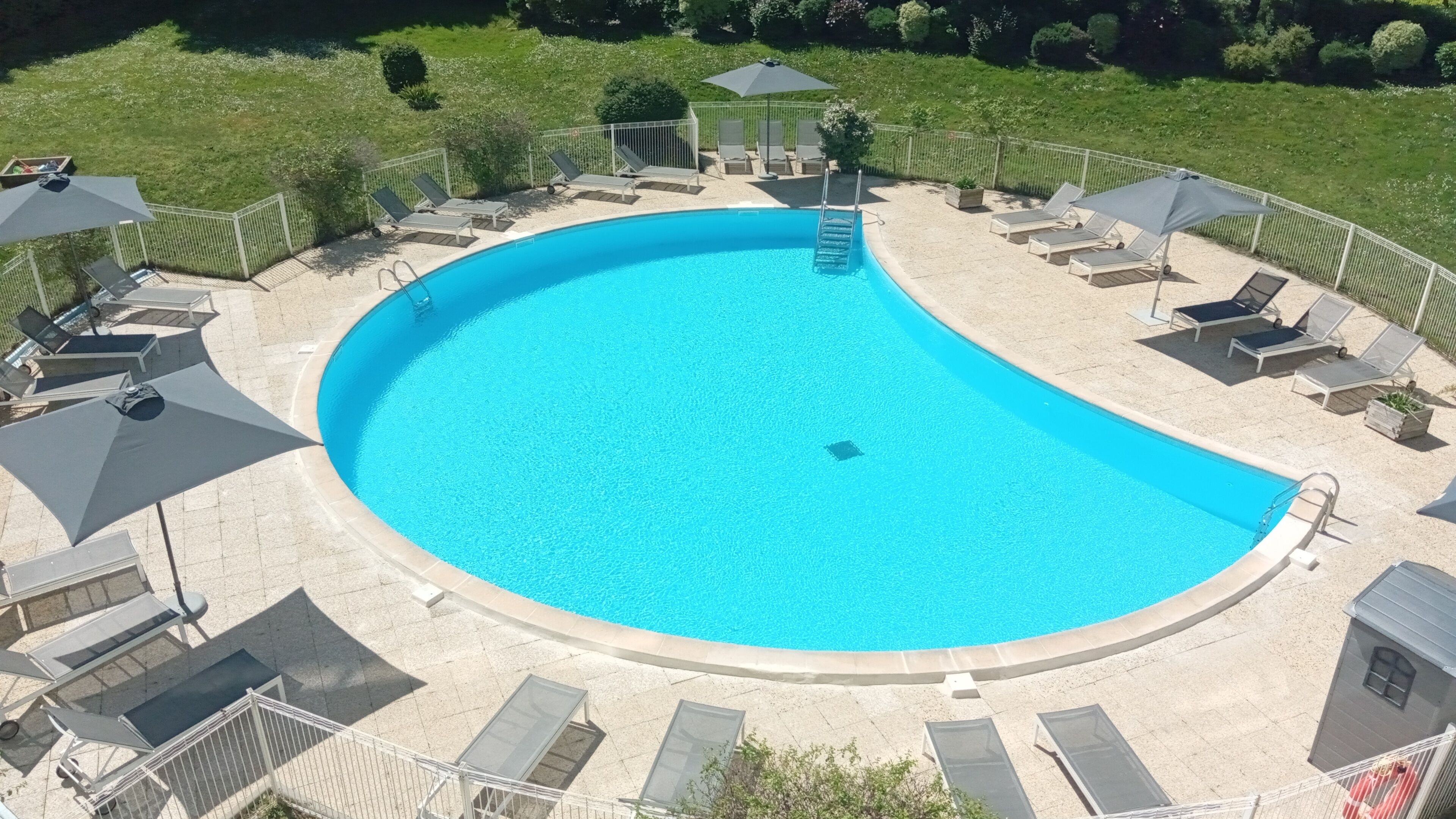 A large, curved swimming pool with a surrounding deck, lounge chairs, and umbrellas.