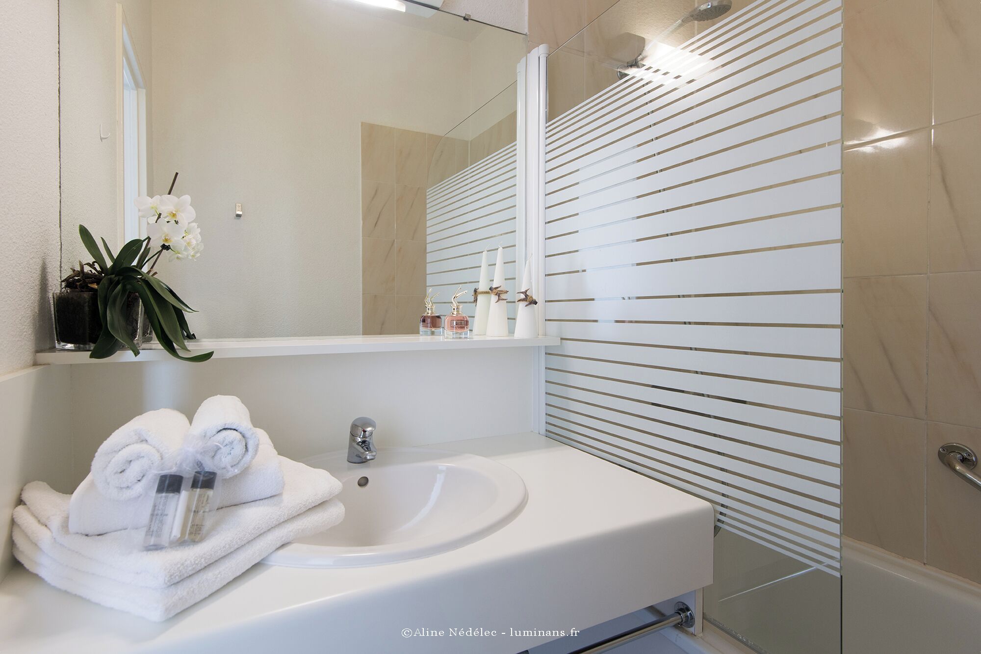 Une salle de bain moderne avec un lavabo blanc, un miroir et une douche équipée de stores horizontaux.