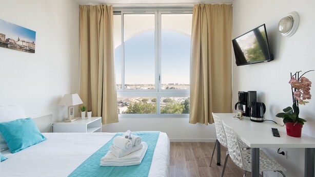 Une chambre d’hôtel avec un lit, un bureau, une télévision et une vue sur la ville.