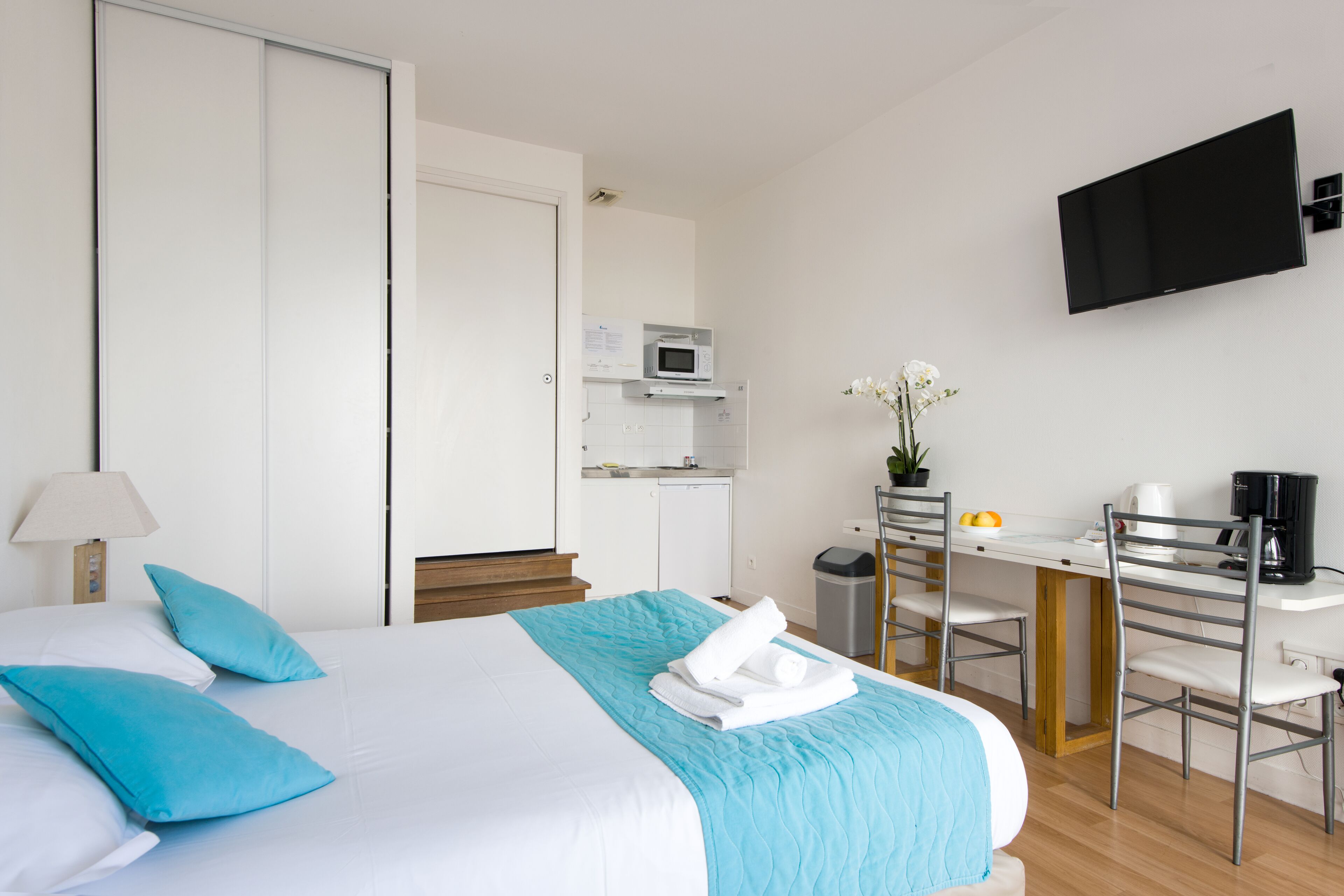 A hotel room with a bed, a desk, a chair, a TV, and a small kitchenette.