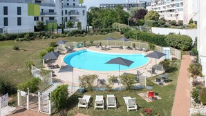 Une piscine entourée de chaises longues et de parasols, avec une clôture et de la verdure en arrière-plan.