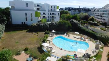 Un edificio residencial con piscina rodeada de sillas de descanso y sombrillas.