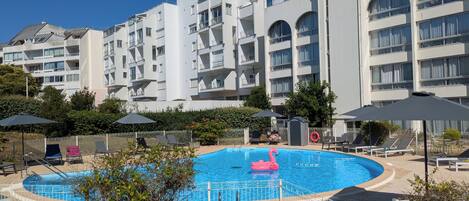 Una piscina con sillas de descanso y sombrillas, rodeada por una valla blanca.