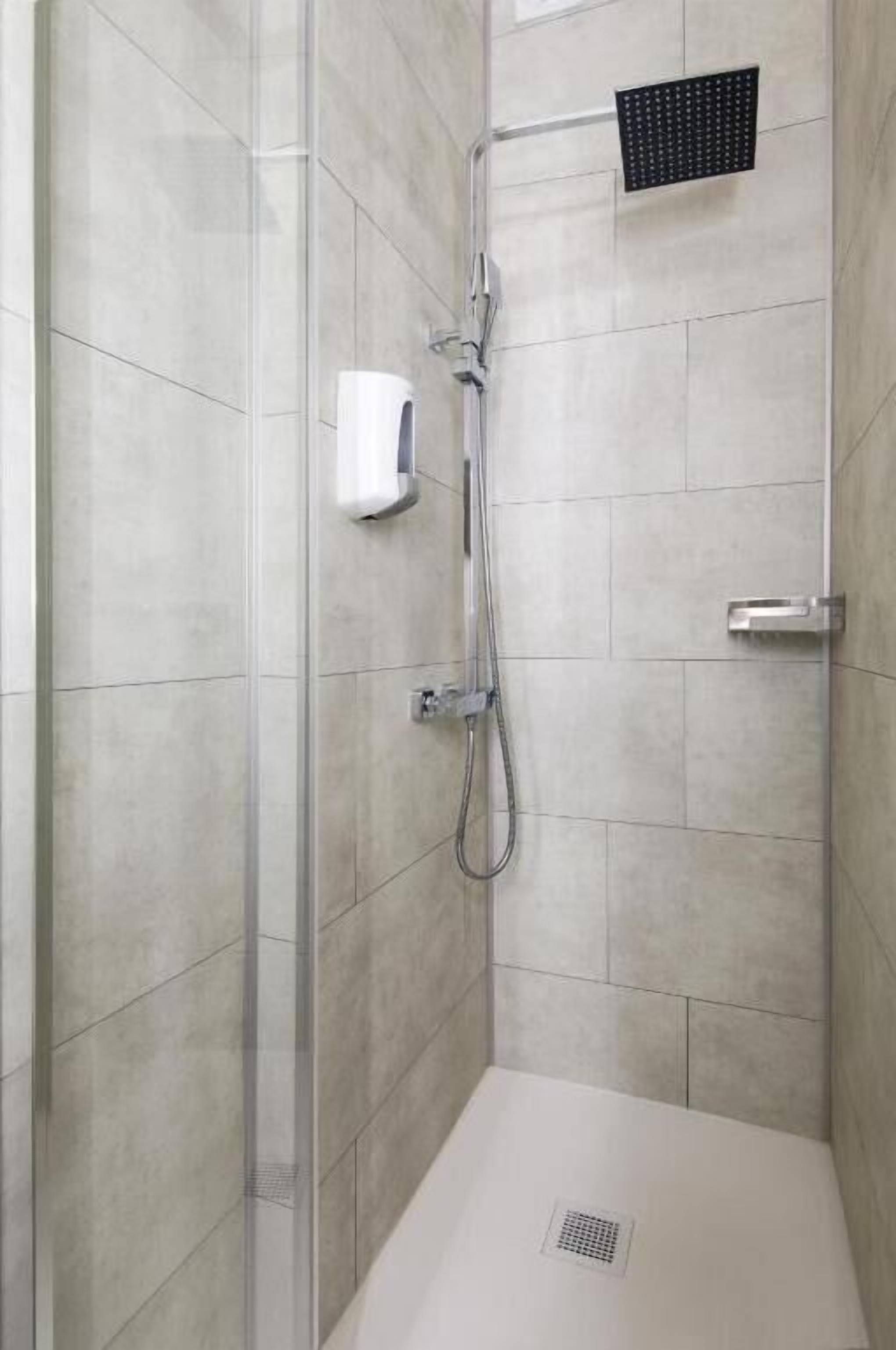 Um chuveiro sem barreiras, com porta de vidro, chuveiro manual, painel de controle na parede e ralo no chão.