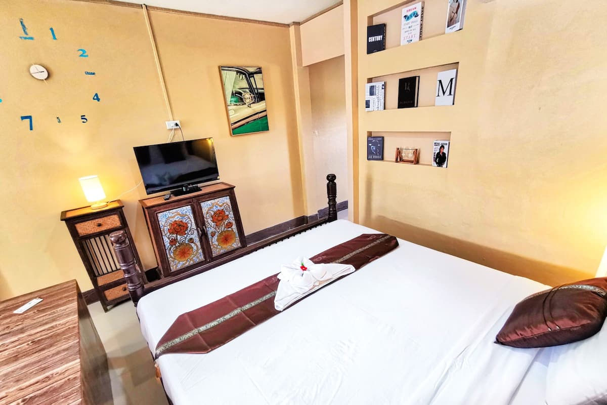 A hotel room with a bed, a television, a bookshelf, and a wall clock.