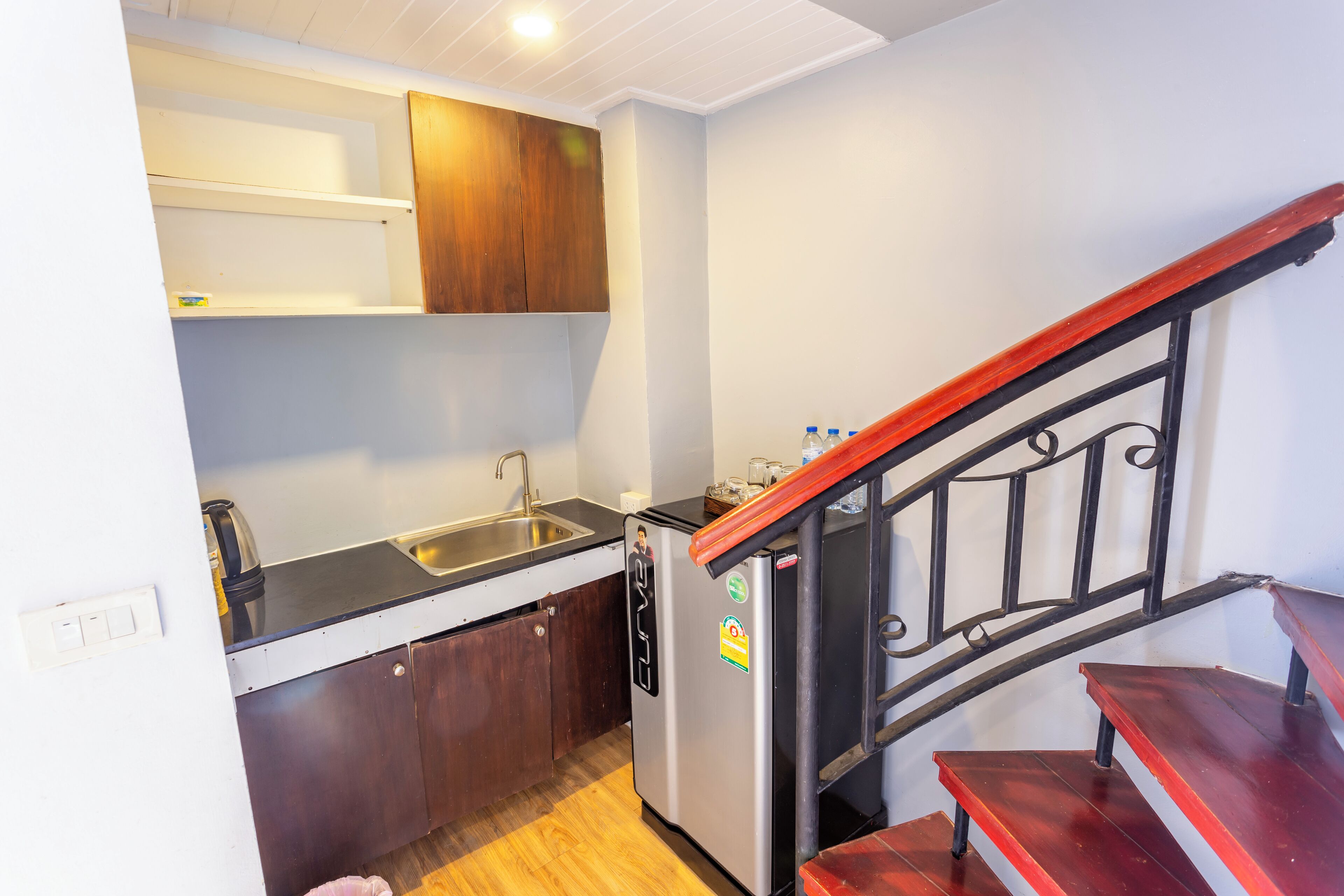 A compact kitchen with a sink, a refrigerator, wooden cabinets, and a wooden staircase.