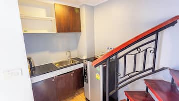 A compact kitchen with a sink, a refrigerator, wooden cabinets, and a wooden staircase.