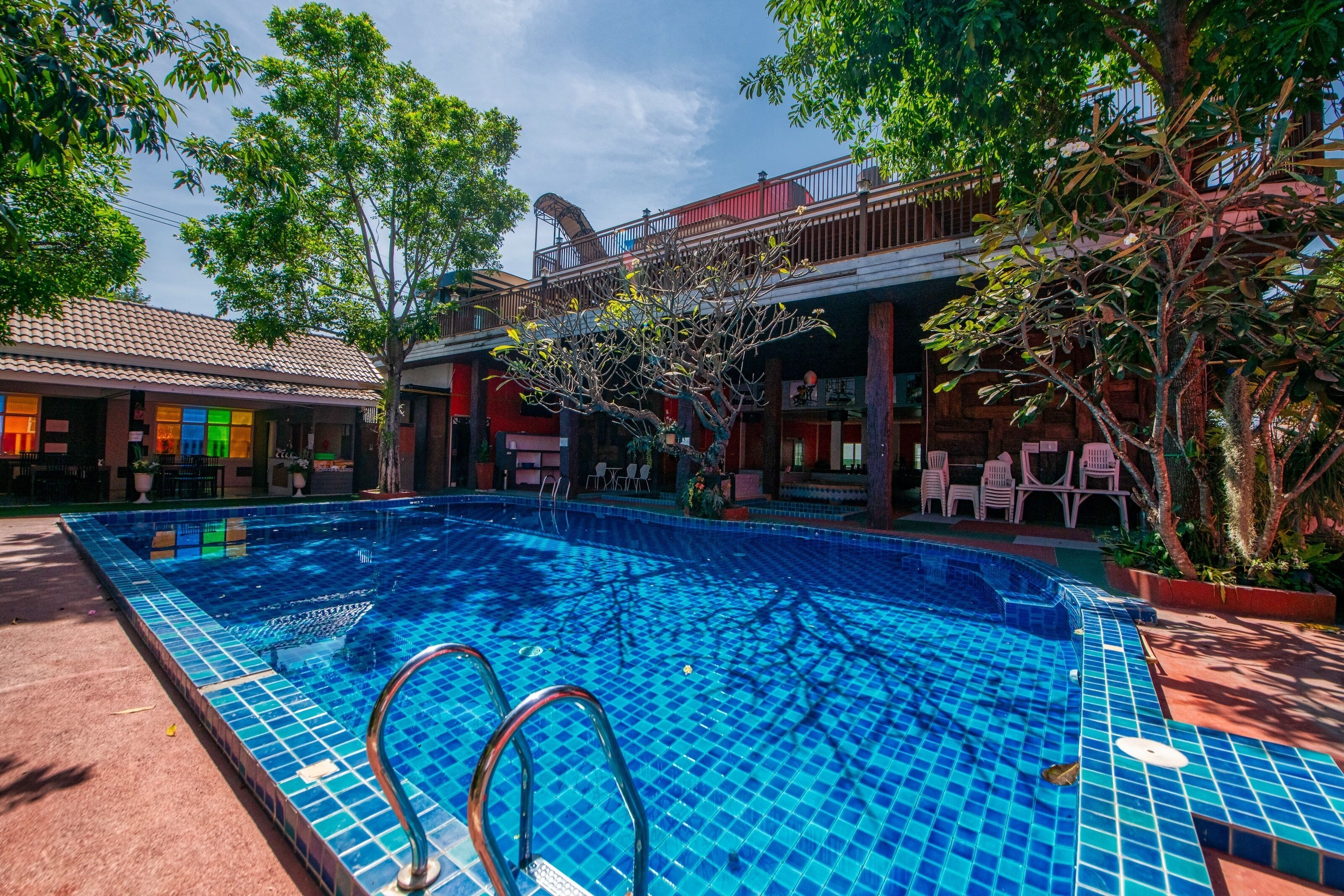 A swimming pool with tiled edges, surrounded by trees and a building with a balcony.