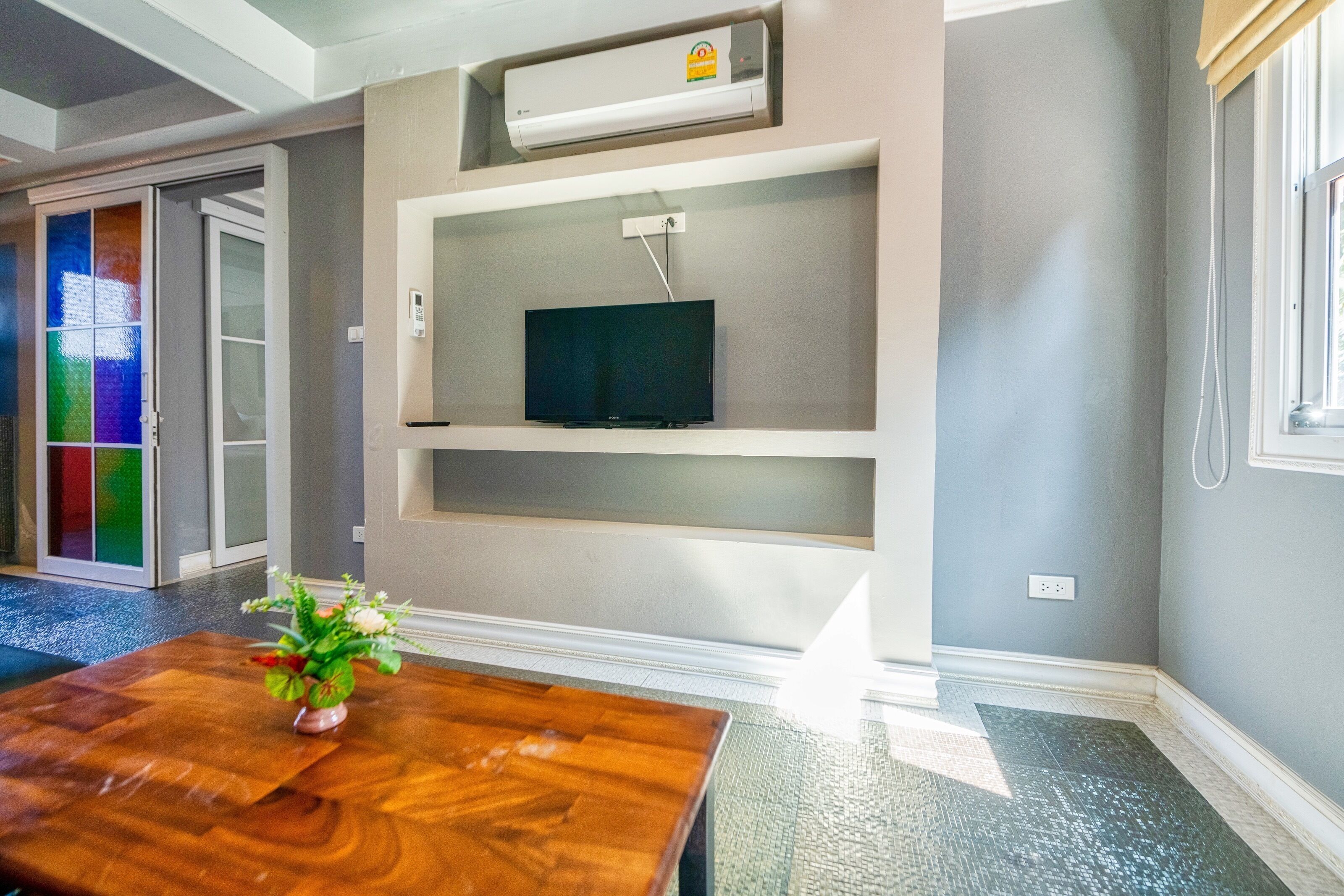 Una sala de estar moderna con una mesa de centro de madera, un televisor de pantalla plana montado en la pared y un ventanal con vidrieras de colores.