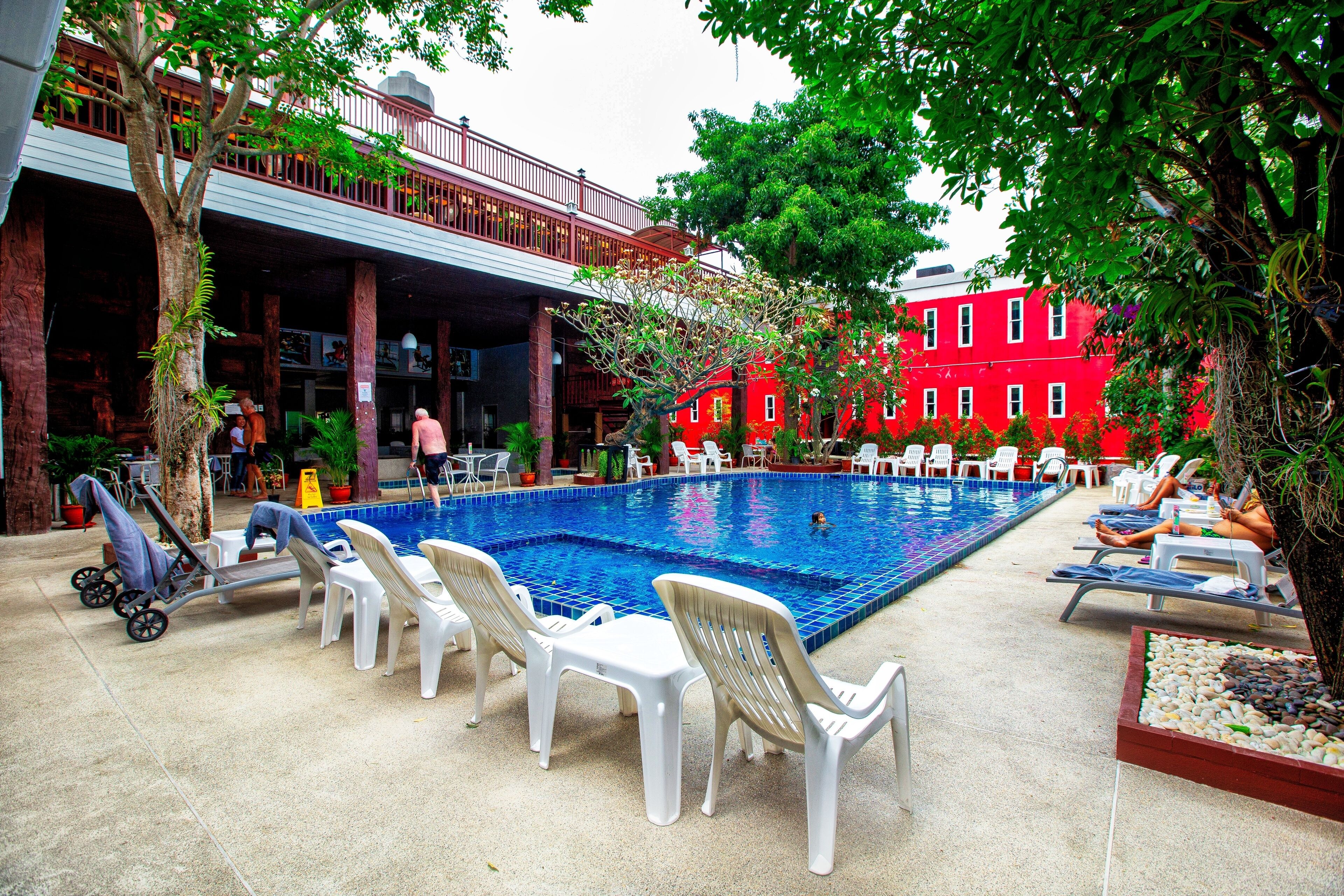 Piscina com espreguiçadeiras e um edifício vermelho ao fundo.