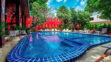 A swimming pool with blue tiles, surrounded by lounge chairs and a red building in the background.