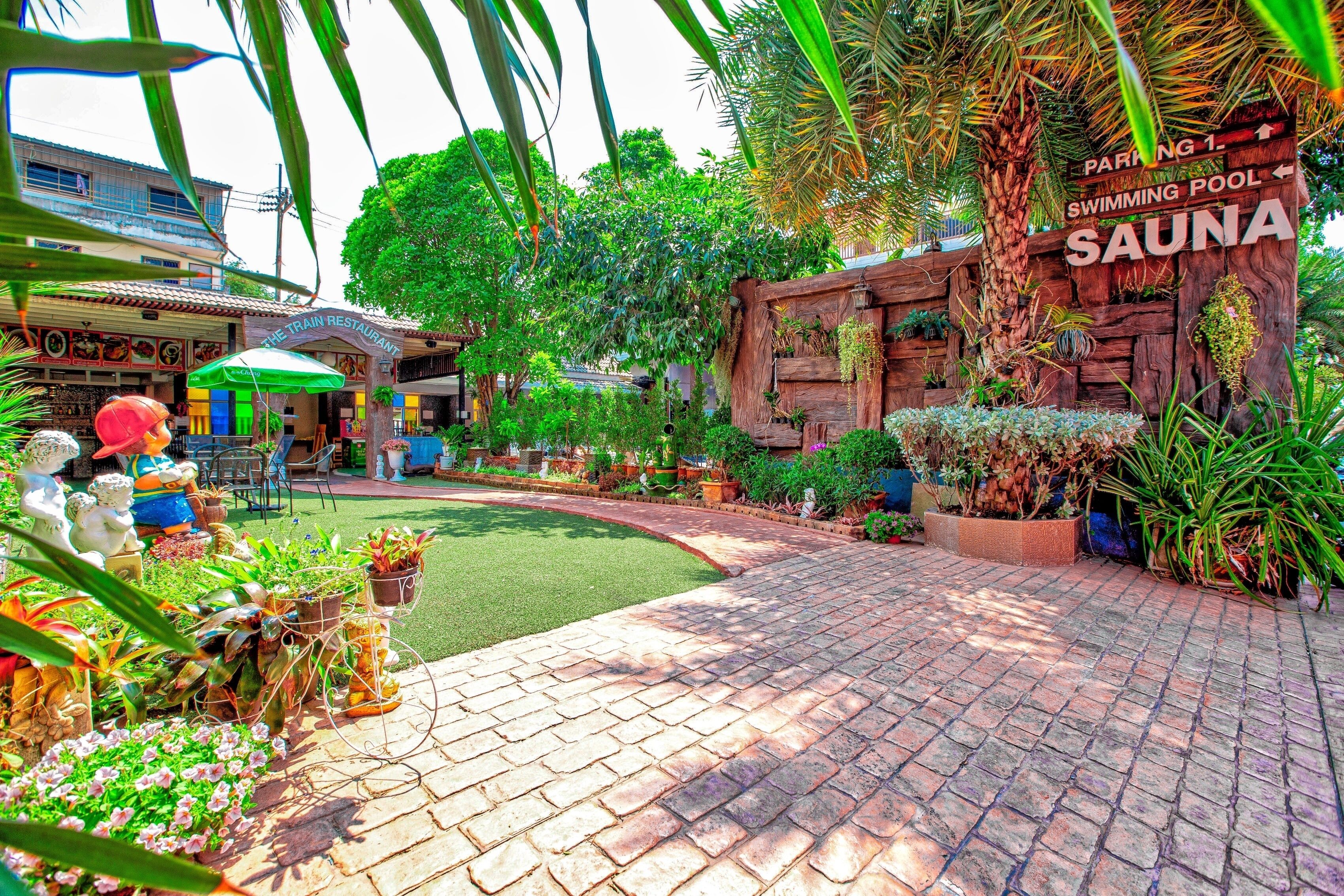 A spa area with a wooden sign indicating a swimming pool and sauna, surrounded by lush greenery and a brick pathway.