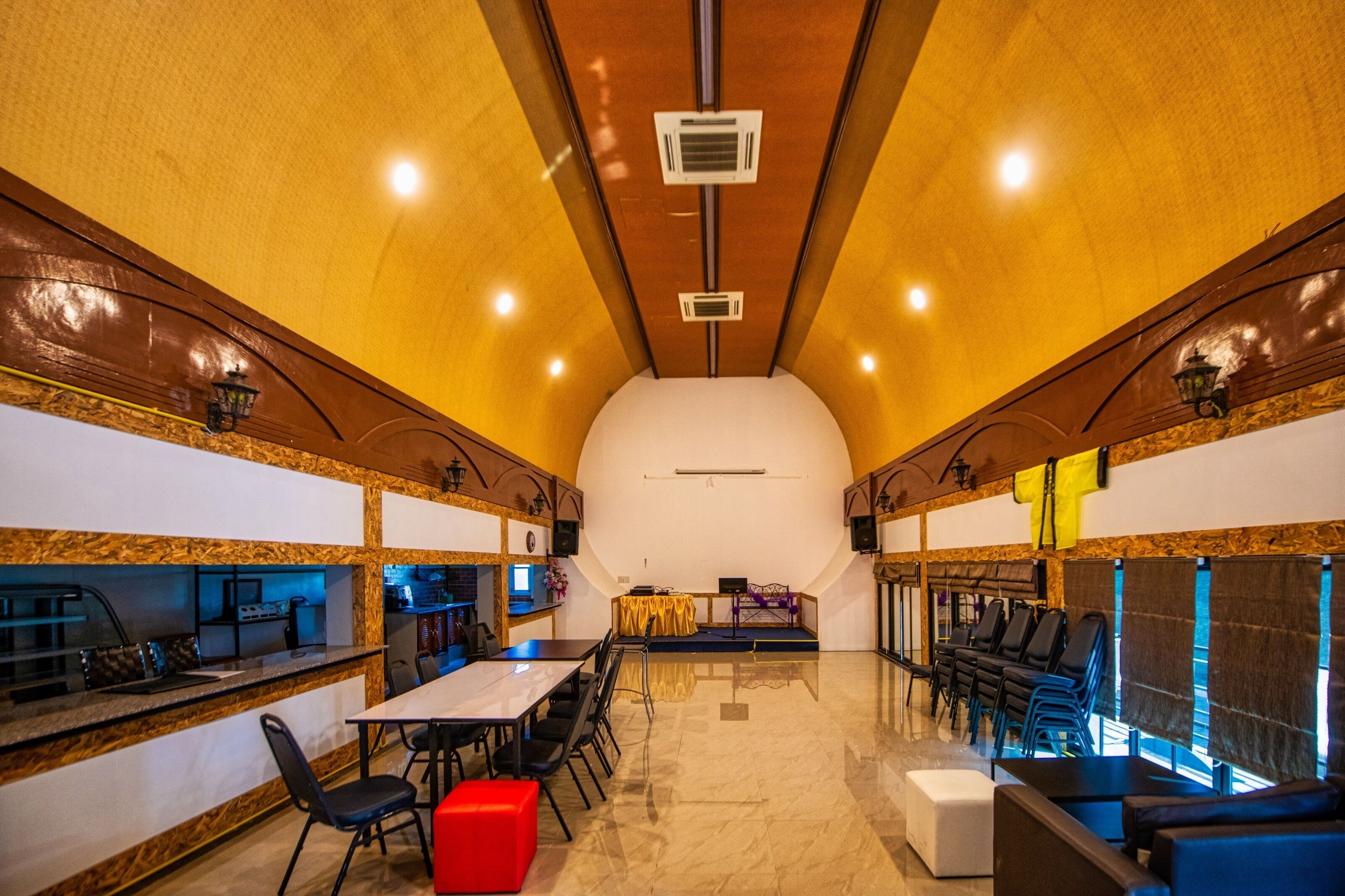 A spacious room with a long table and chairs, a stage, and a seating area with couches.