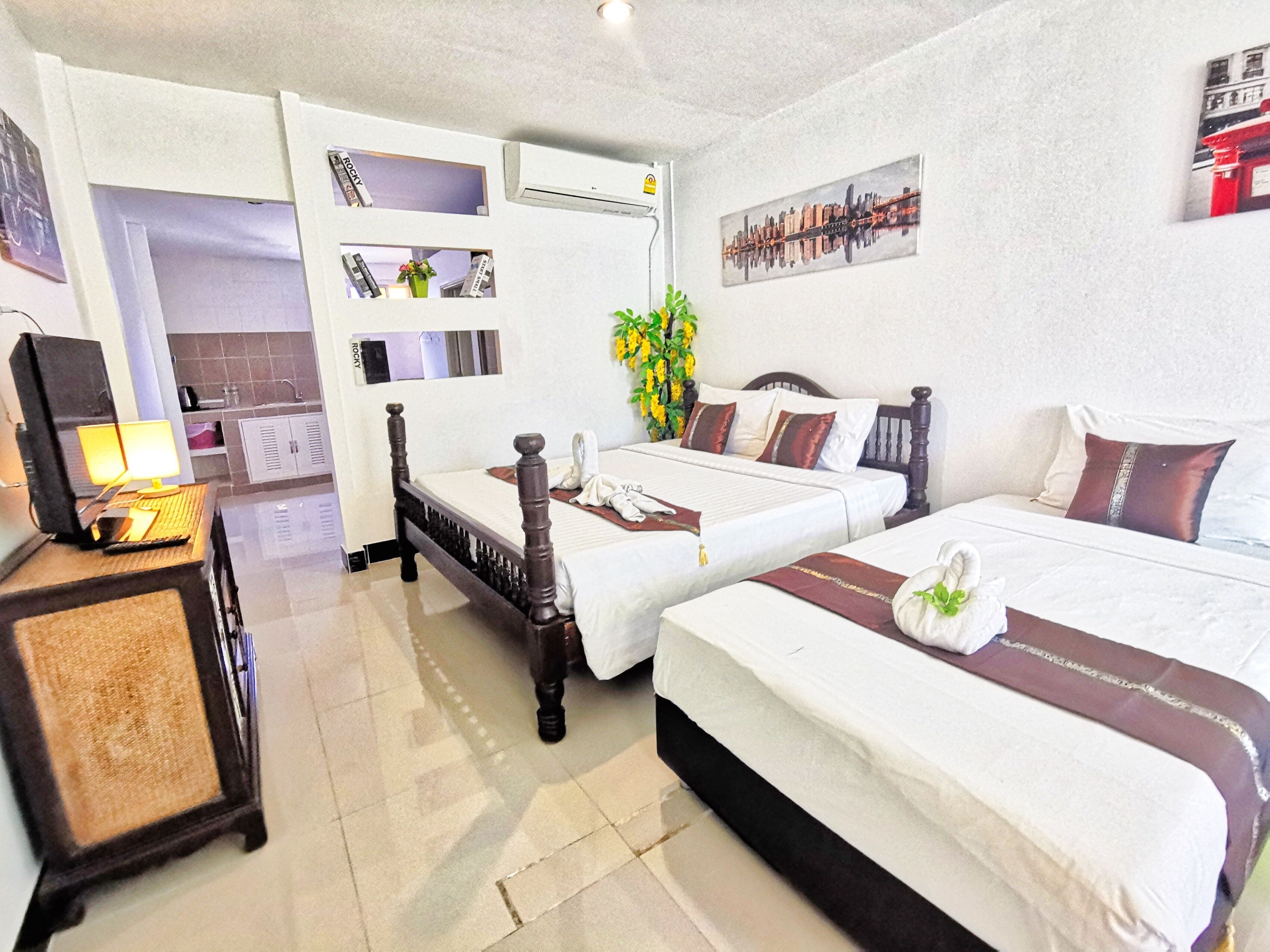A hotel room with two single beds, a desk with a lamp, a small plant, and a cityscape painting on the wall.