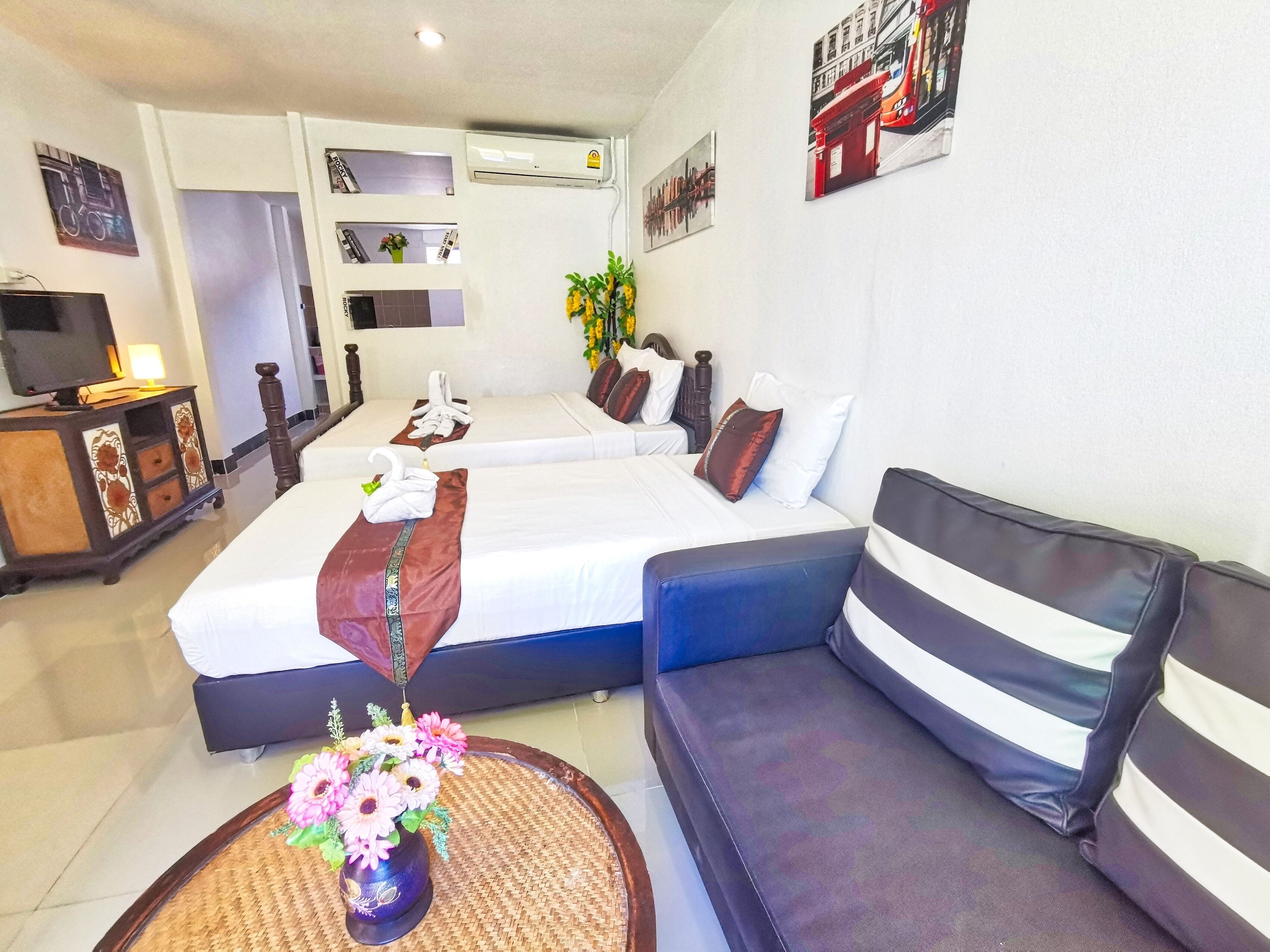 Ein Hotelzimmer mit zwei Betten, einem Sofa, einem Fernseher und einer Blumenvase.
