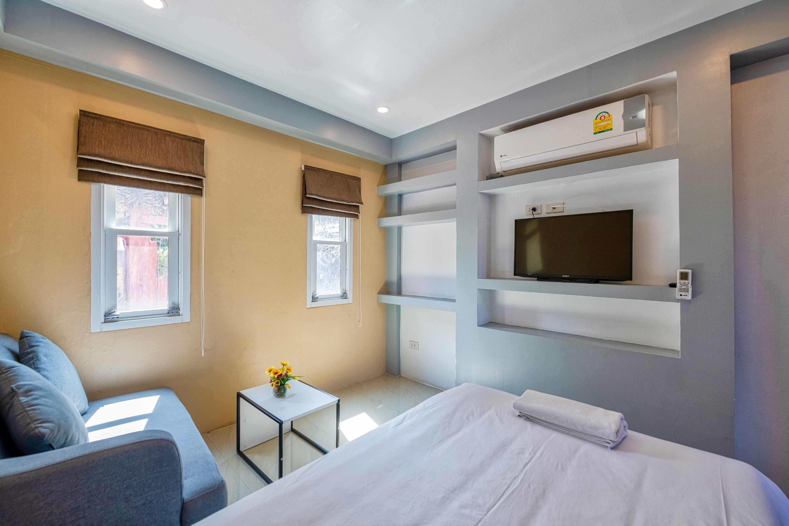 Een hotelkamer met een bed, een bank, een kleine tafel met bloemen en een aan de muur bevestigde televisie.