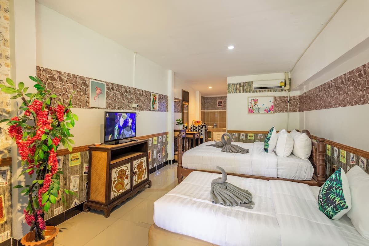 A hotel room with two beds, a television, a potted plant, and a bathroom visible in the background.