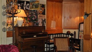 Une pièce chaleureuse avec un piano en bois, un canapé en velours rouge, une lampe et un mur décoré de divers affiches, ainsi qu’un meuble en bois.