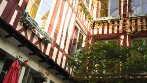 Un bâtiment traditionnel à colombages, doté d’un balcon, de plantes en pot et d’un espace extérieur aménagé pour s’asseoir.