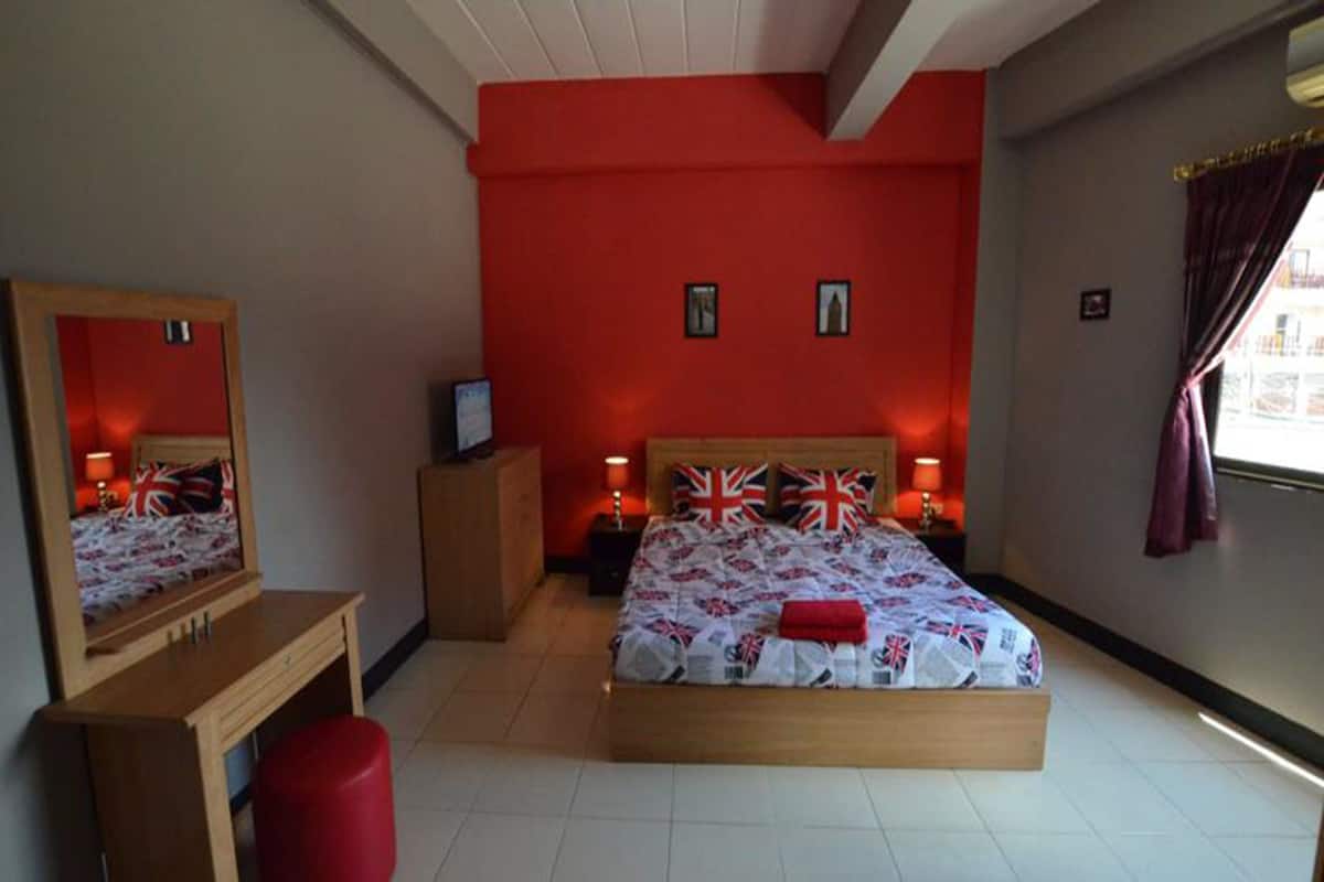 A bedroom with a bed, a desk, a chair, and a mirror.